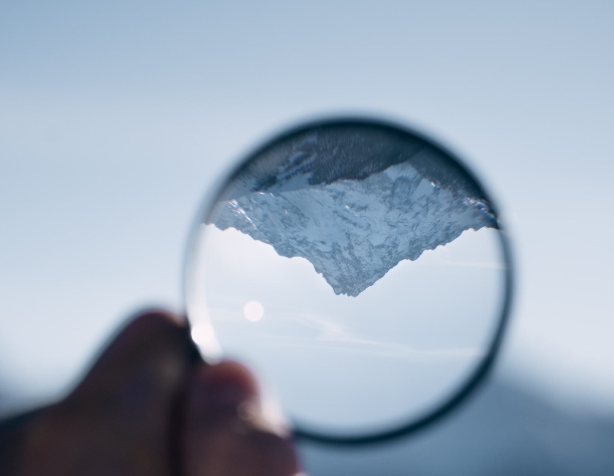 man holding a glass ball that shows an upside down snow covered mountain