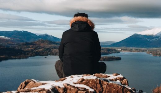 man sitting on a rock looking at mountains
